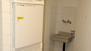 A compact laundry room with a front-loading washing machine, a sink, and a tiled floor. - Nest - Baarerstrasse 55 (Zug)
