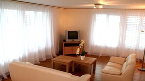 A living room with a sofa, a coffee table, and a television on a stand. - Nest - Baarerstrasse 55 (Zug)