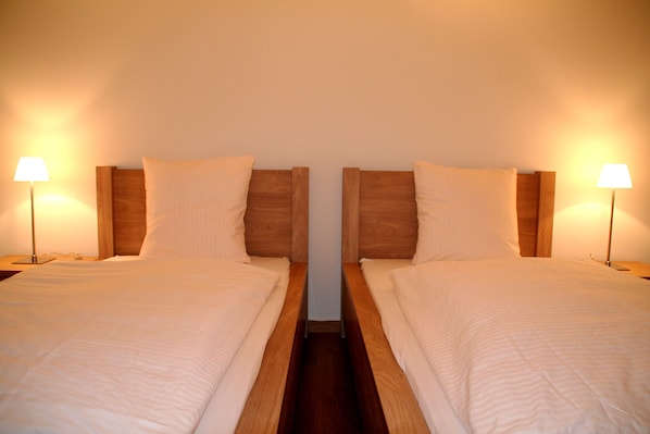 A symmetrical room with two beds, each with a wooden headboard and a bedside lamp. - Nest - Baarerstrasse 55 (Zug)