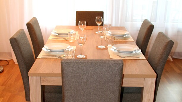 A dining table set for six with chairs, a wooden floor, and a window with curtains. - Nest - Baarerstrasse 55 (Zug)