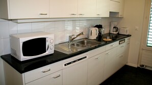 A modern kitchen with white cabinets, a black countertop, a microwave, a coffee maker, and a toaster. - Nest - Baarerstrasse 55 (Zug)
