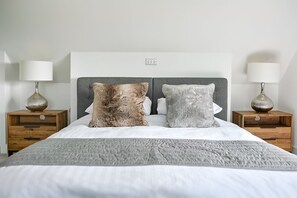 A neatly made bed with two pillows, a grey throw blanket, and two bedside tables with lamps. - Groeslon -  Luxury cottages (Menai Bridge)
