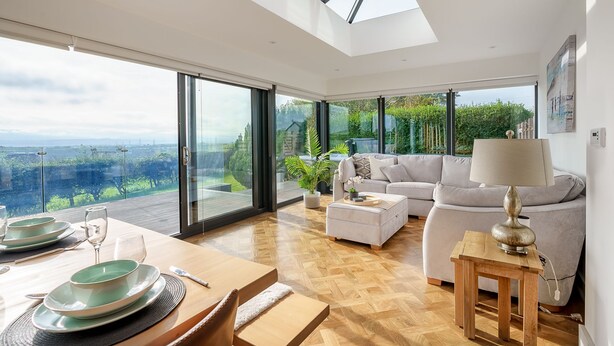 A spacious living room with a large glass door leading to a balcony, a sofa, a coffee table, and a dining area with a table set for two.