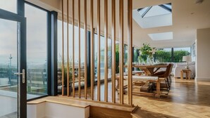 A modern interior with a wooden staircase, a dining area with a view, and a living space with a sofa and lamp.