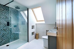 A modern bathroom with a glass shower enclosure, a skylight, a white toilet, and a wooden door. - Groeslon -  Luxury cottages (Menai Bridge)
