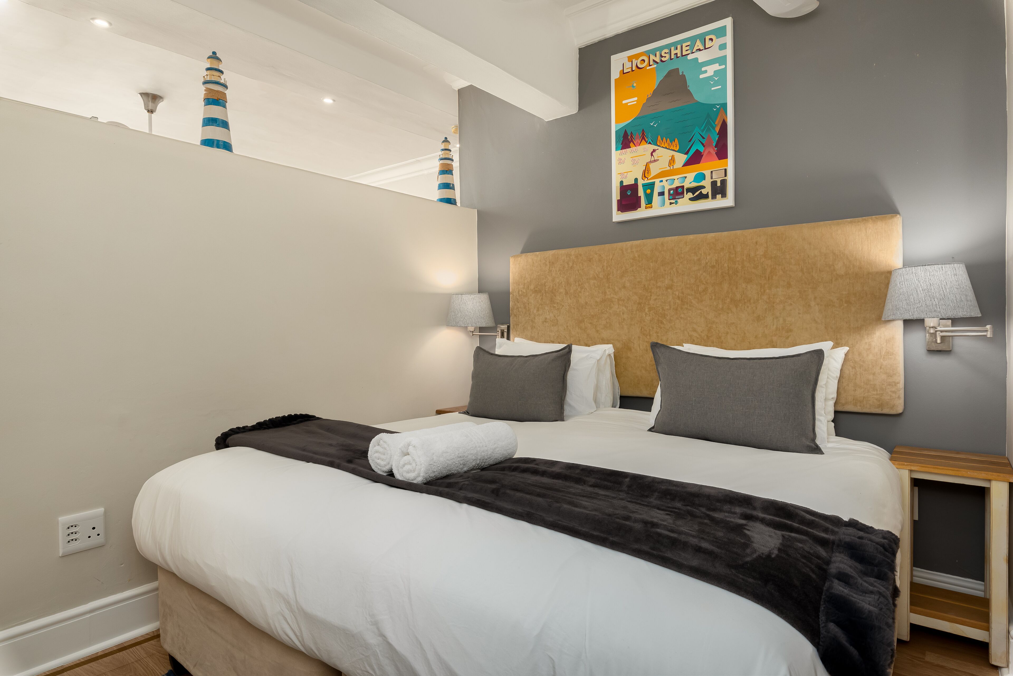 A modern hotel room with a large bed, grey walls, and a lighthouse artwork.