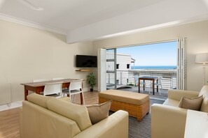 A modern living room with a sofa, a dining table, and a TV. There is a balcony with a view of the sea. - Caprice Court 6 (Cape Town)