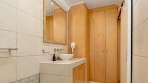 A bathroom with a wooden vanity, a white sink, a mirror, and a shower area. - Caprice Court 6 (Cape Town)