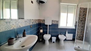 Et badeværelse med håndvask, toilet, bidét og bruser.