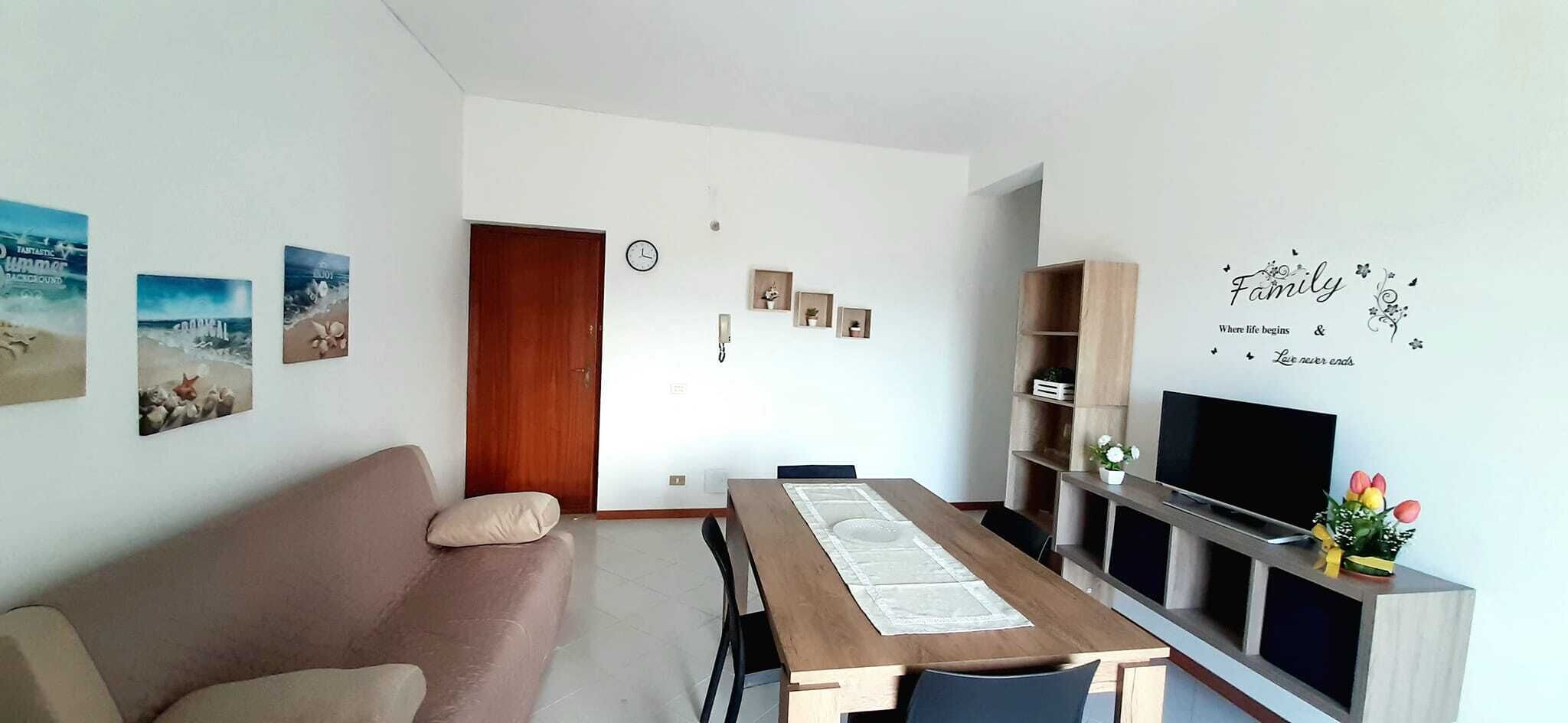 A modern living room with a sofa, dining table, TV, and decorative wall art.