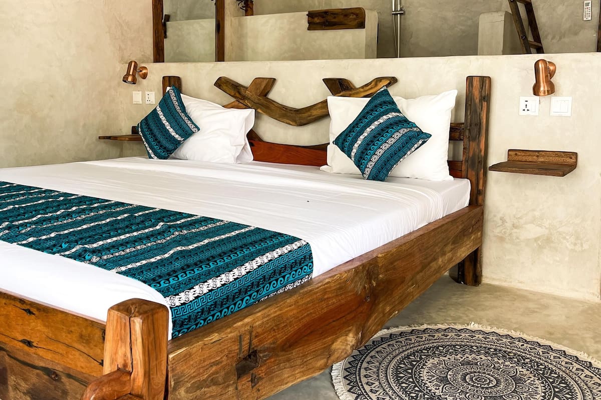Quarto com cama de madeira, tapete redondo estampado e luminária pendente.
