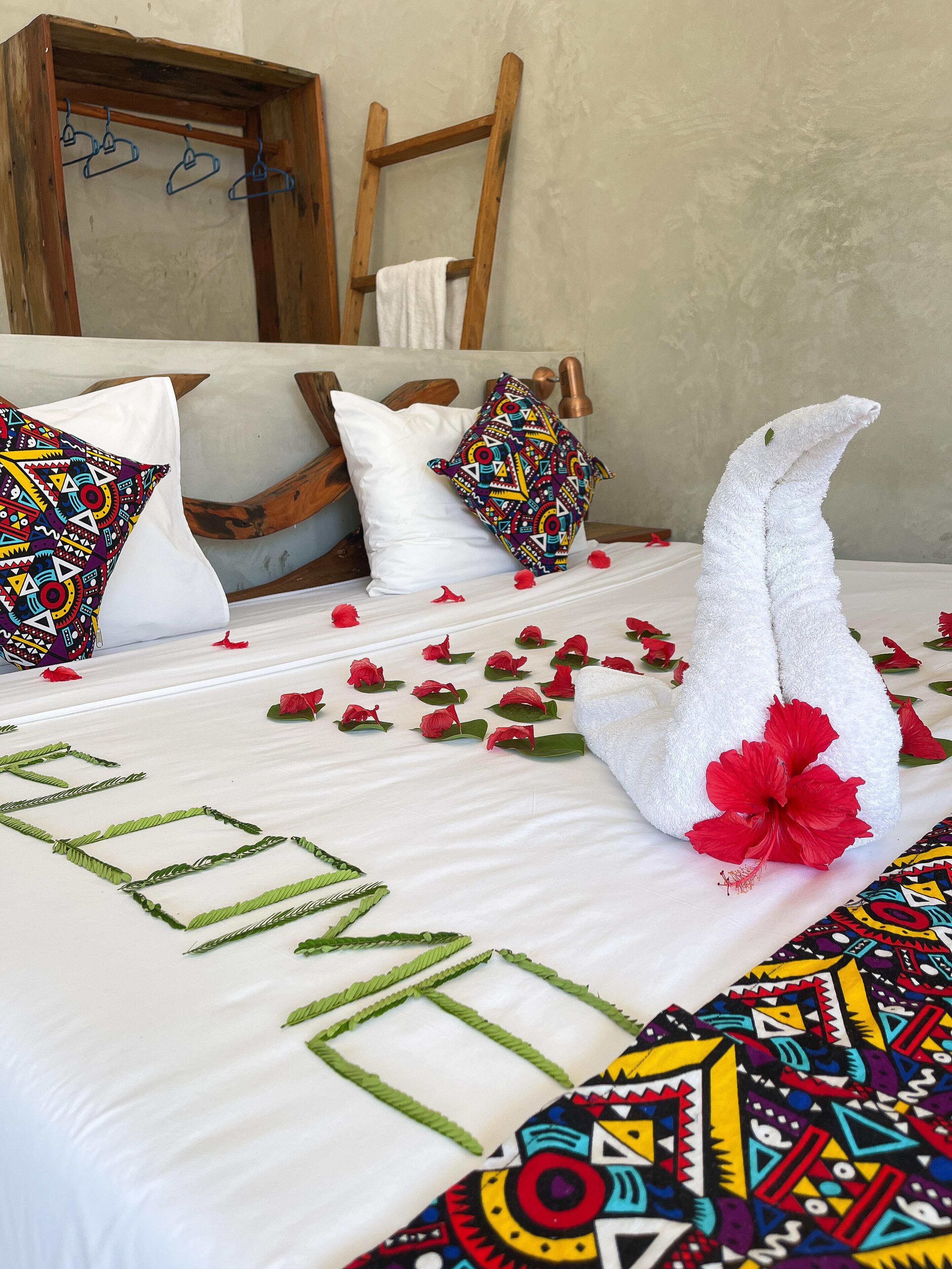 A neatly made bed with a towel shaped like a swan, red flowers, and a colorful pillow.