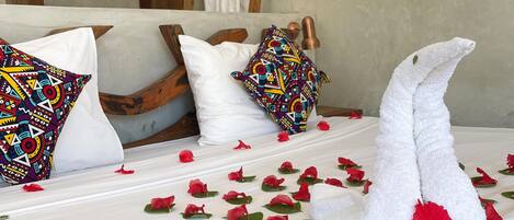 A neatly made bed with a towel shaped like a swan, red flowers, and a colorful pillow.