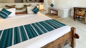 A spacious bedroom with a large bed, wooden headboard, and a wooden nightstand. There is a small table and a chair in the corner. - Mambo Cabana (Pwani Mchangani)