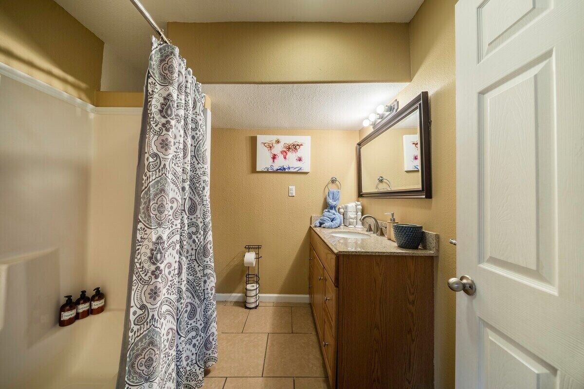 Un baño con cortina de ducha, lavamanos, espejo y toallero.