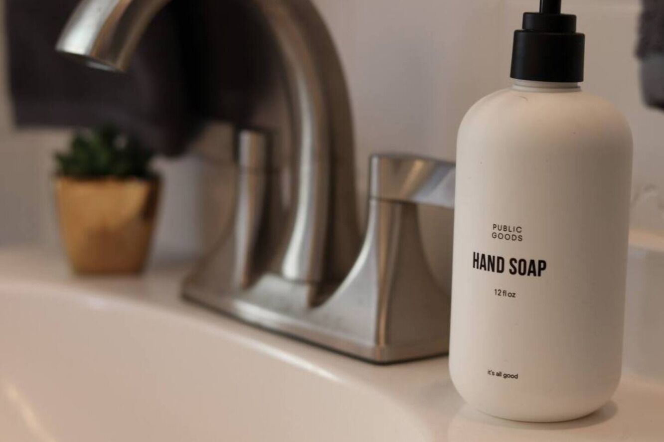Una bottiglia di sapone per le mani su un ripiano del bagno, vicino a un rubinetto.