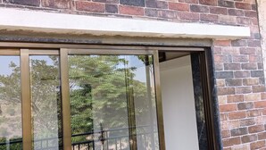 A room with a brick wall, a large sliding glass door, and a red chair. - Vue Villa (Igatpuri)