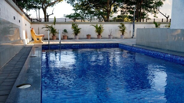 A swimming pool with a tiled edge, a sun lounger, and potted plants along the wall. - Vue Villa (Igatpuri)