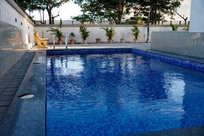 A swimming pool with a tiled edge, a sun lounger, and potted plants along the wall. - Vue Villa (Igatpuri)