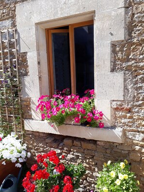 A stone building with a window featuring a wooden frame and a flower box with pink and red flowers.