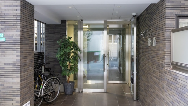 A modern building entrance with a glass door, a potted plant, and bicycles parked outside. - The Premium Namba Minami  (Osaka)