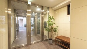 A modern hotel entrance with a glass door, a potted plant, and a wooden bench. - The Premium Namba Minami  (Osaka)