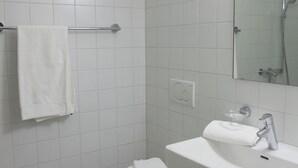 Une salle de bain moderne avec des carreaux blancs, des toilettes, un lavabo et une douche.