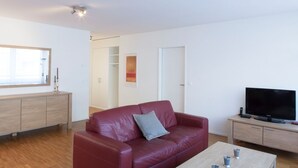 Un salon moderne avec un canapé en cuir rouge, une table basse en bois, un téléviseur à écran plat et un meuble bas en bois au design minimaliste.