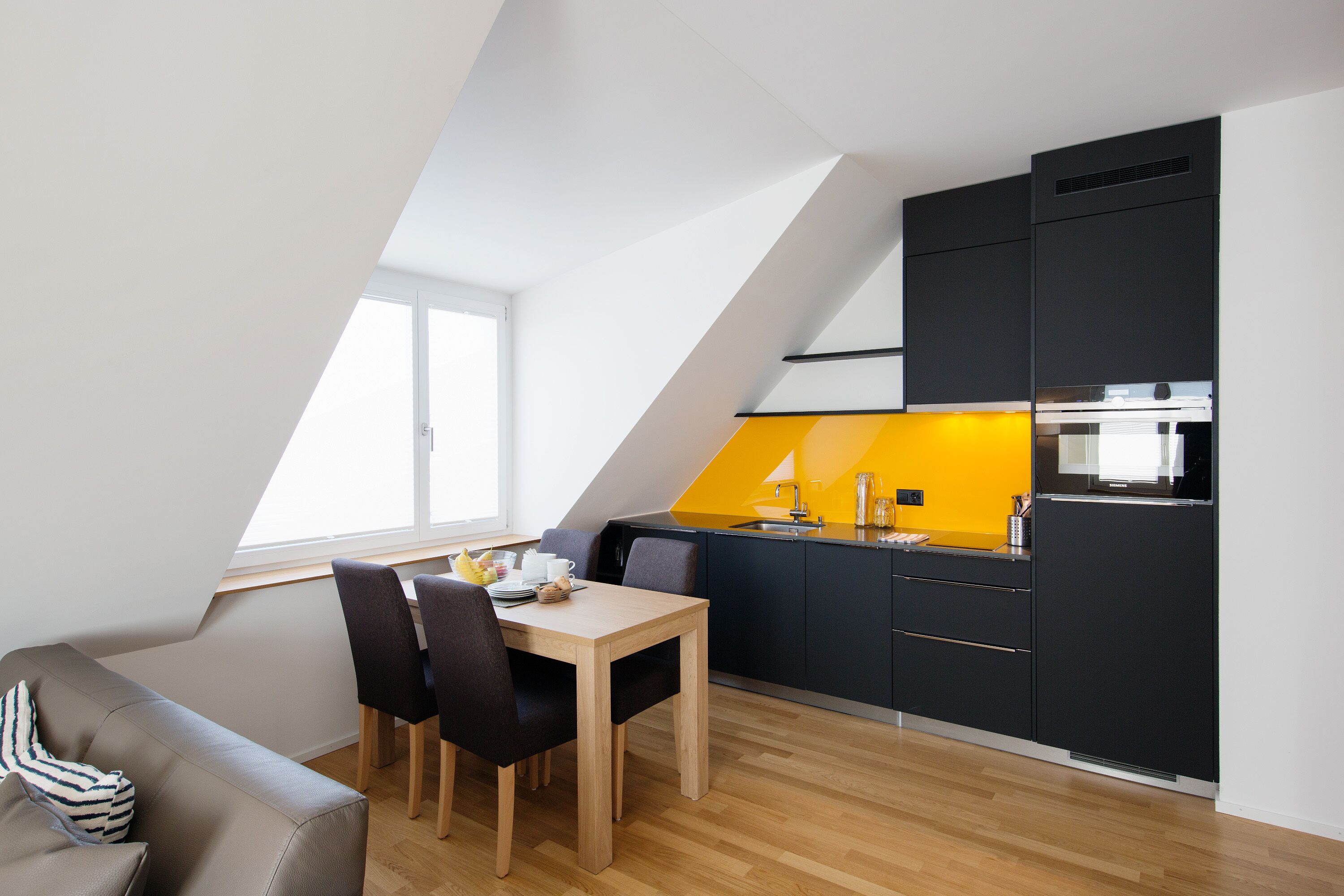 A modern kitchen with black cabinets, a wooden dining table, and a yellow accent wall.