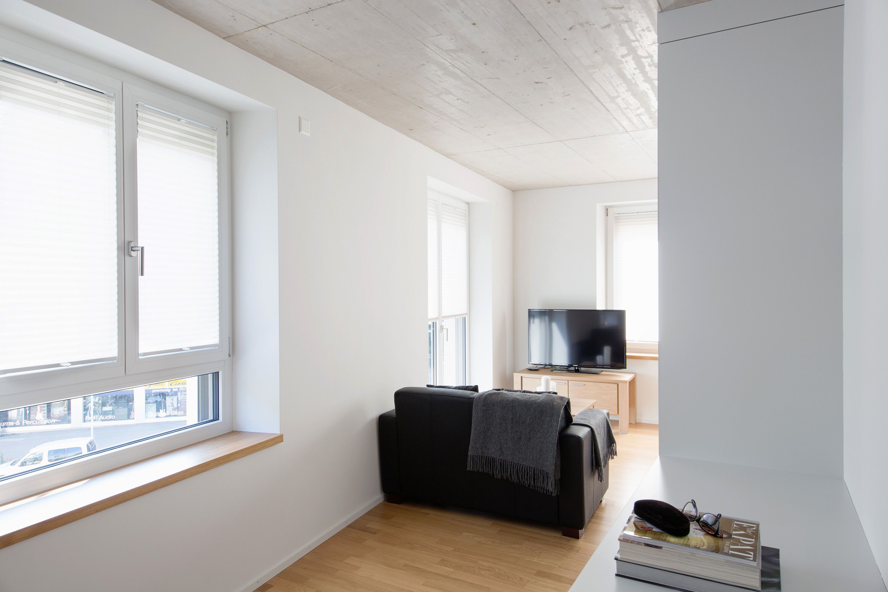 Una sala moderna con un sofá negro, un televisor y una ventana con persianas.