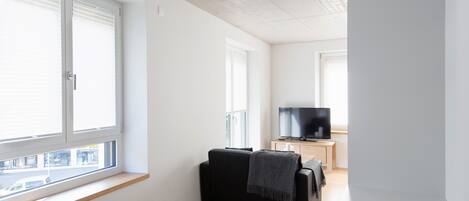 Una sala moderna con un sofá negro, un televisor y una ventana con persianas.