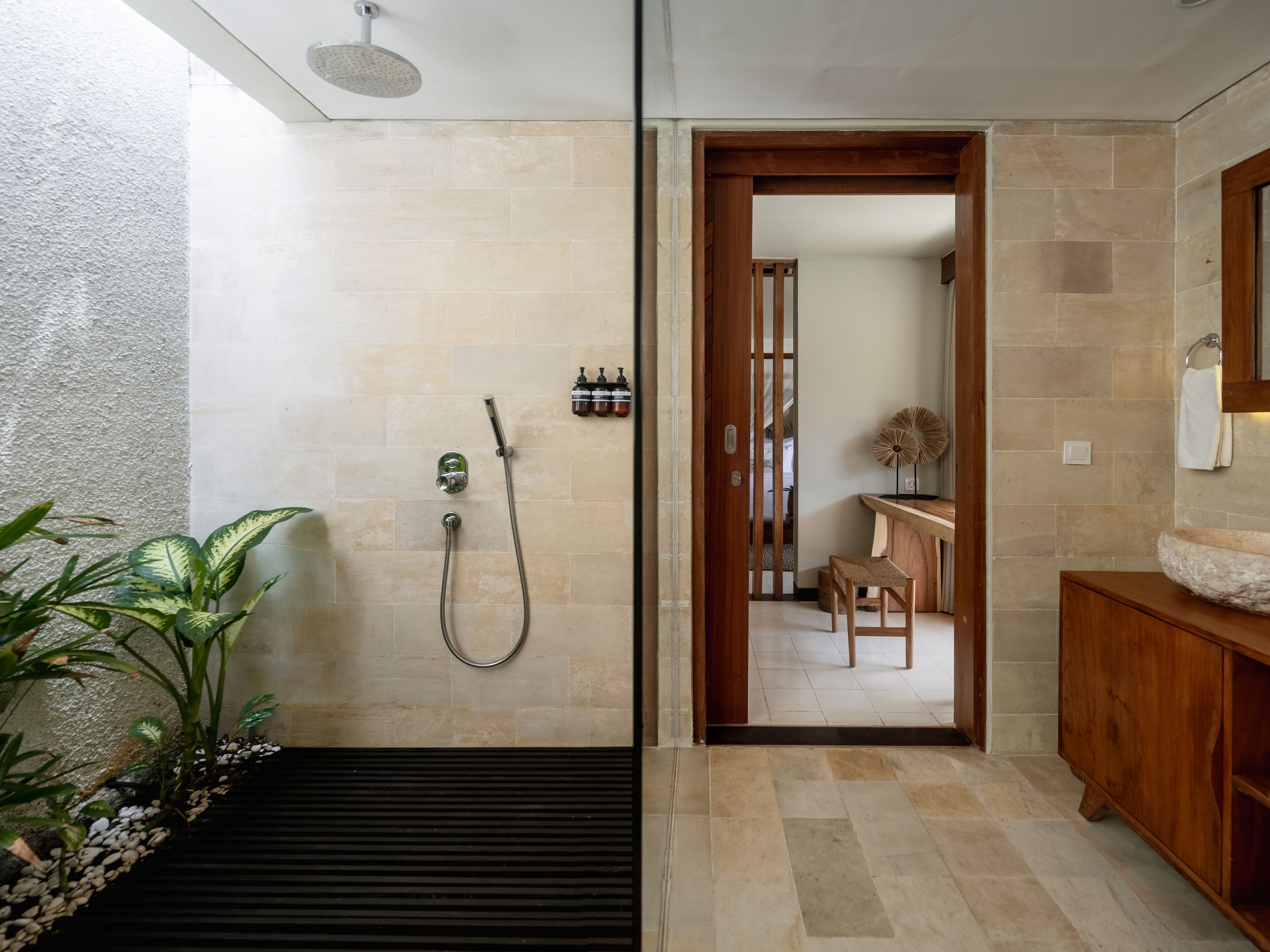 A bathroom with a shower, a wooden door leading to a hallway, and a plant.