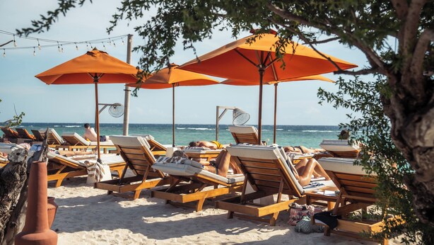 A beach with wooden lounge chairs and orange umbrellas, arranged in rows facing the ocean. - Cocana Resort Gili Trawangan (Gili Trawangan)