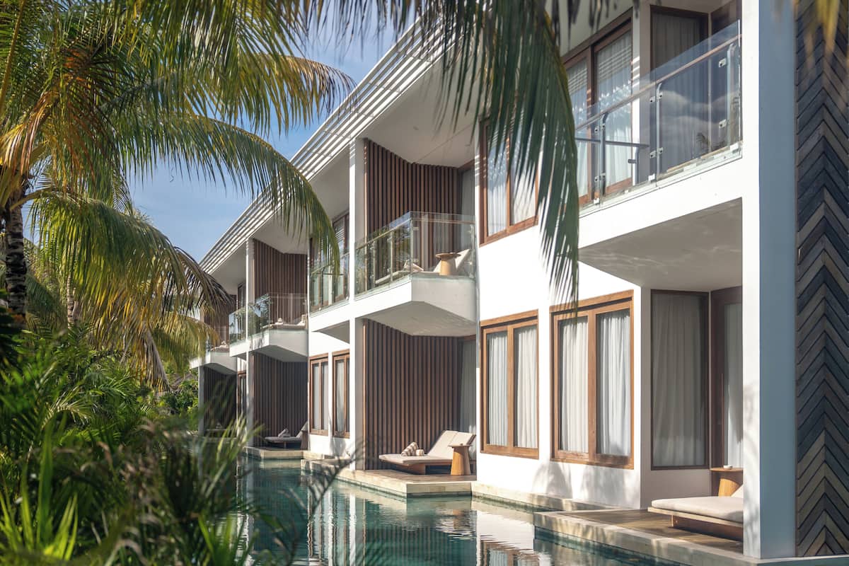 A modern hotel with a pool, multiple balconies, and lush greenery.