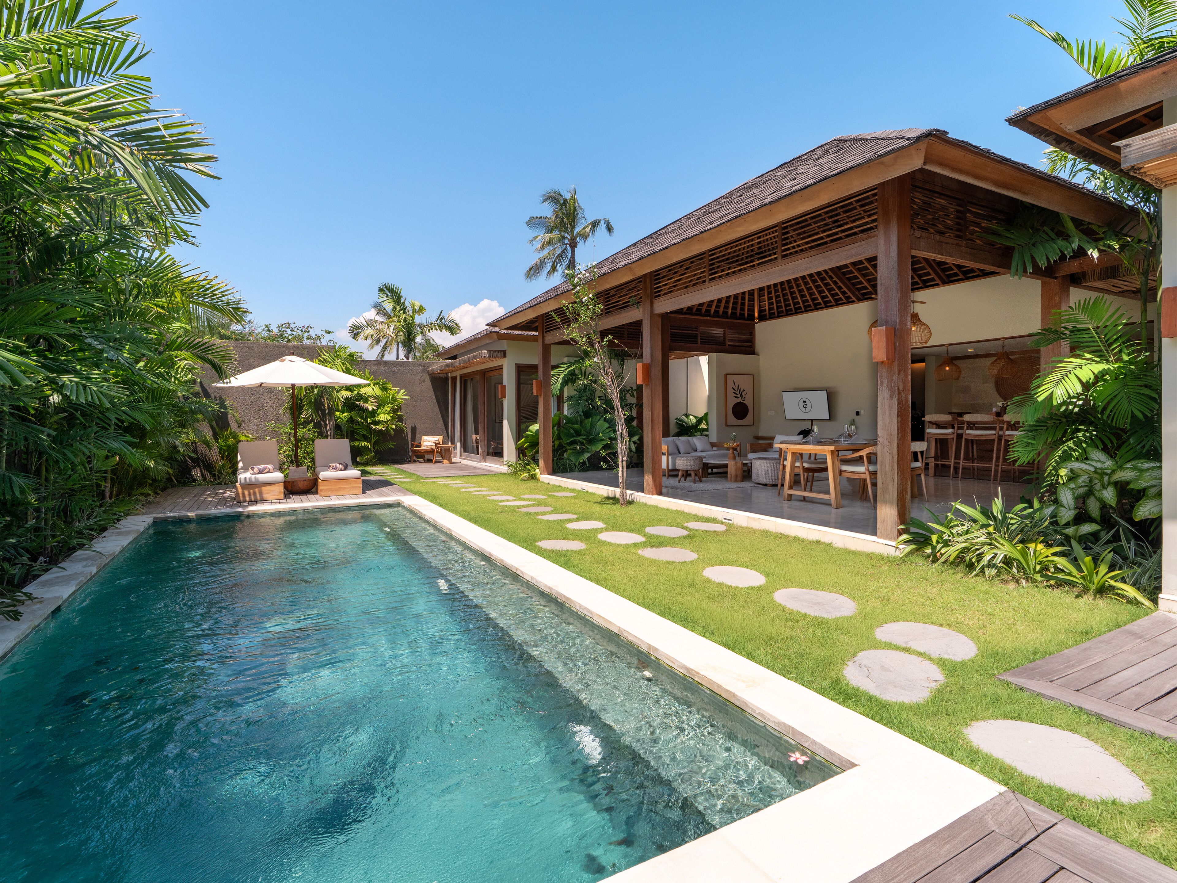 A pool area with a clear blue pool, a wooden deck, and a covered seating area with outdoor furniture.