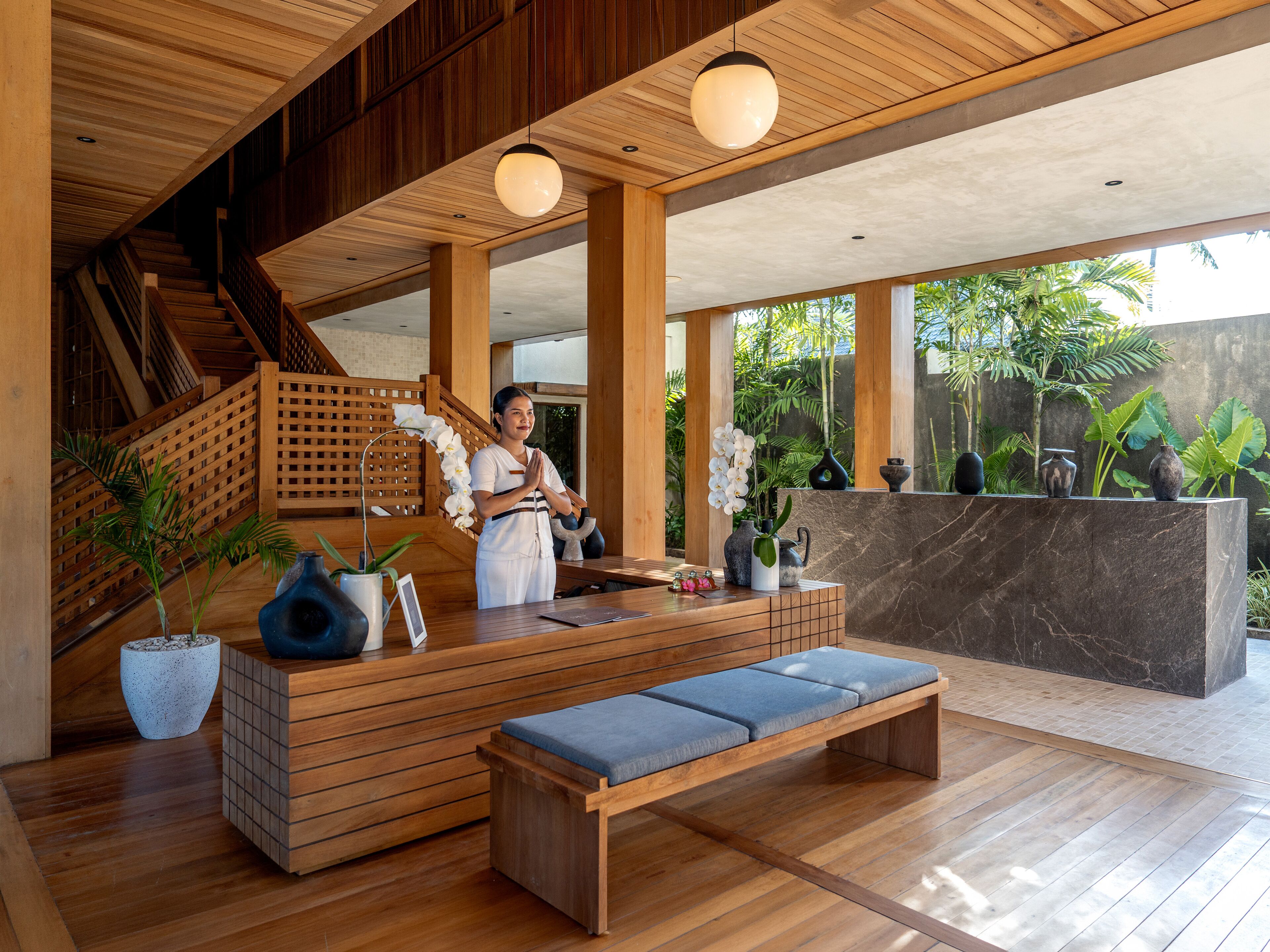 Un área de recepción con un banco de madera, un recepcionista y una escalera.
