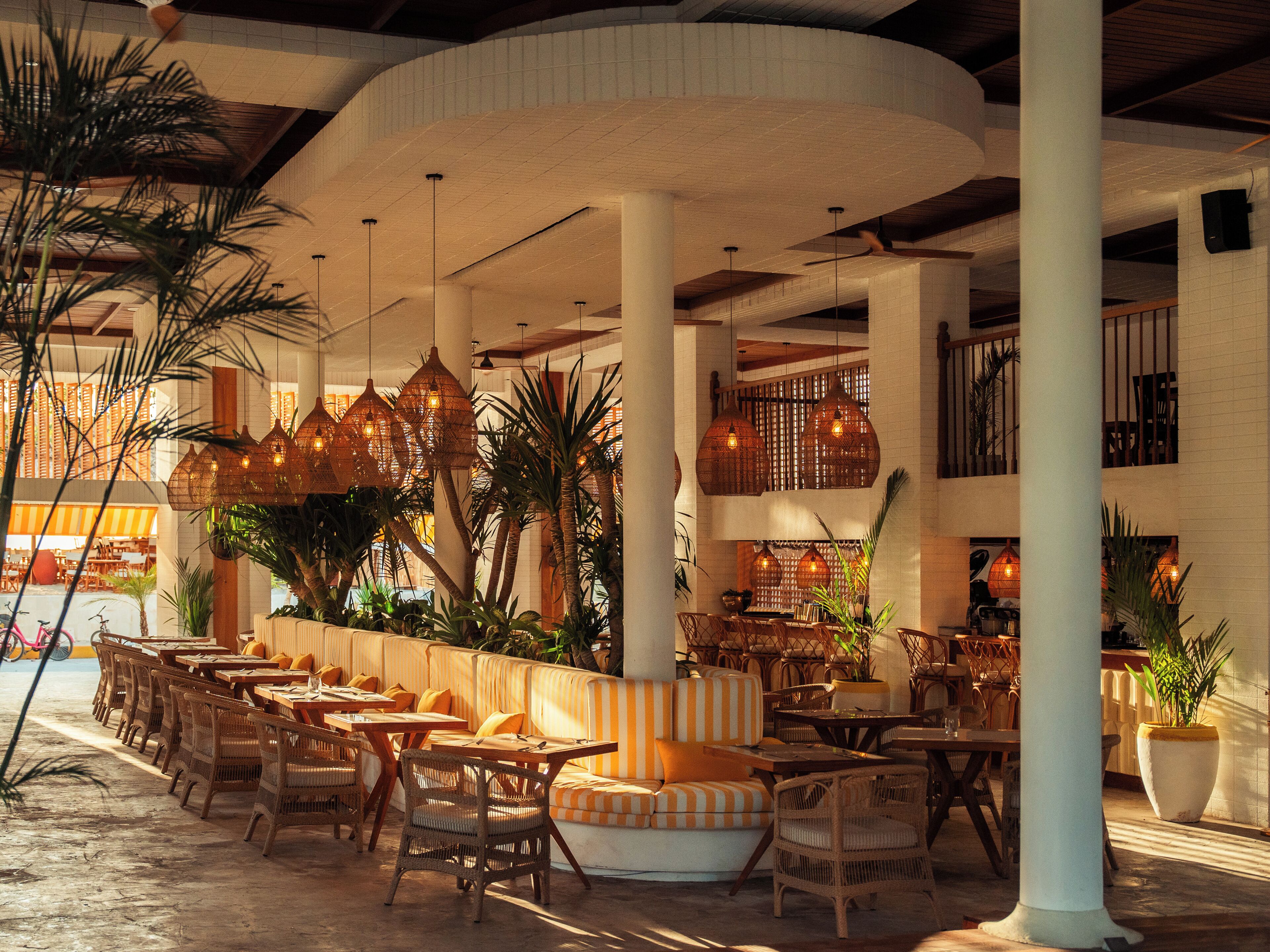 A spacious indoor area with multiple seating arrangements, including sofas and tables, surrounded by large pillars and hanging light fixtures.