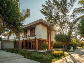 Una casa moderna de dos pisos con techo plano, contraventanas de madera y un jardín con diversas plantas y un camino.