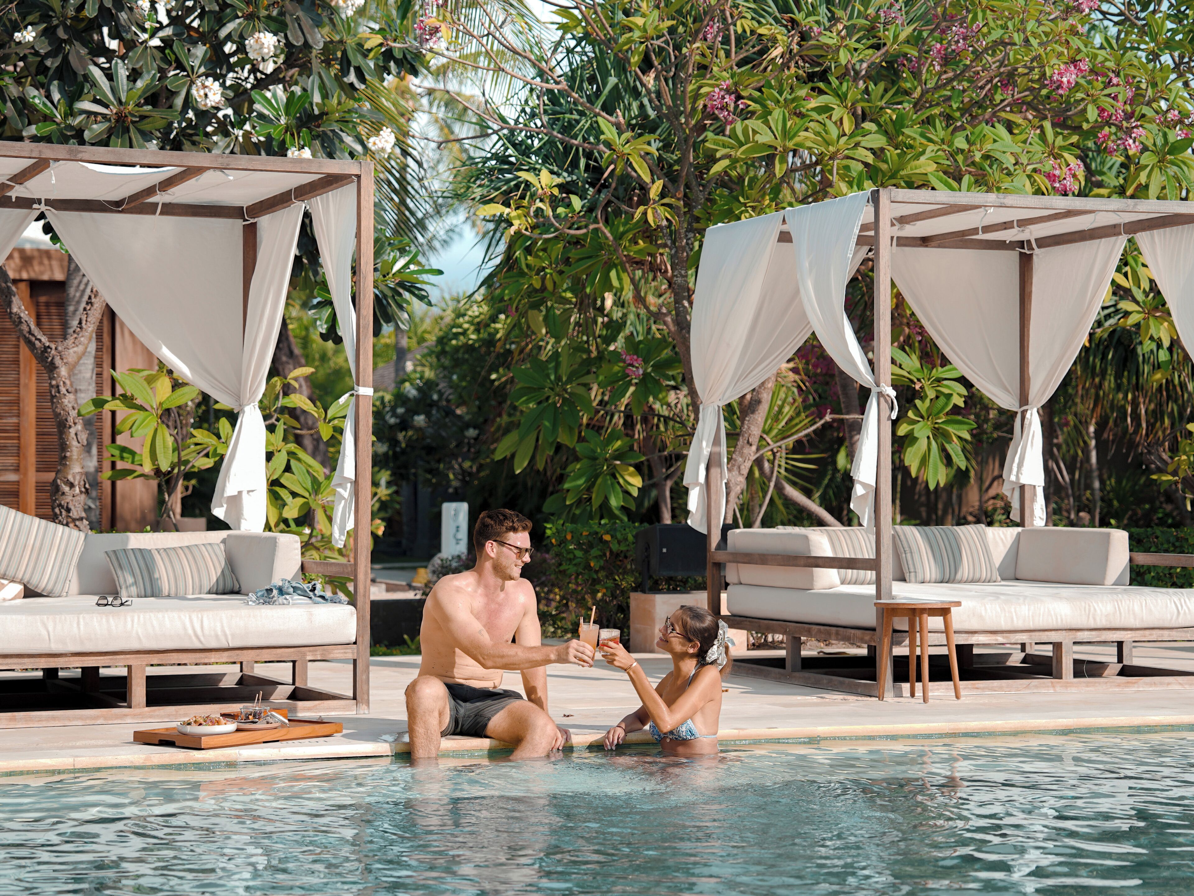 A man and a child in a pool with a wooden deck and lounge chairs.