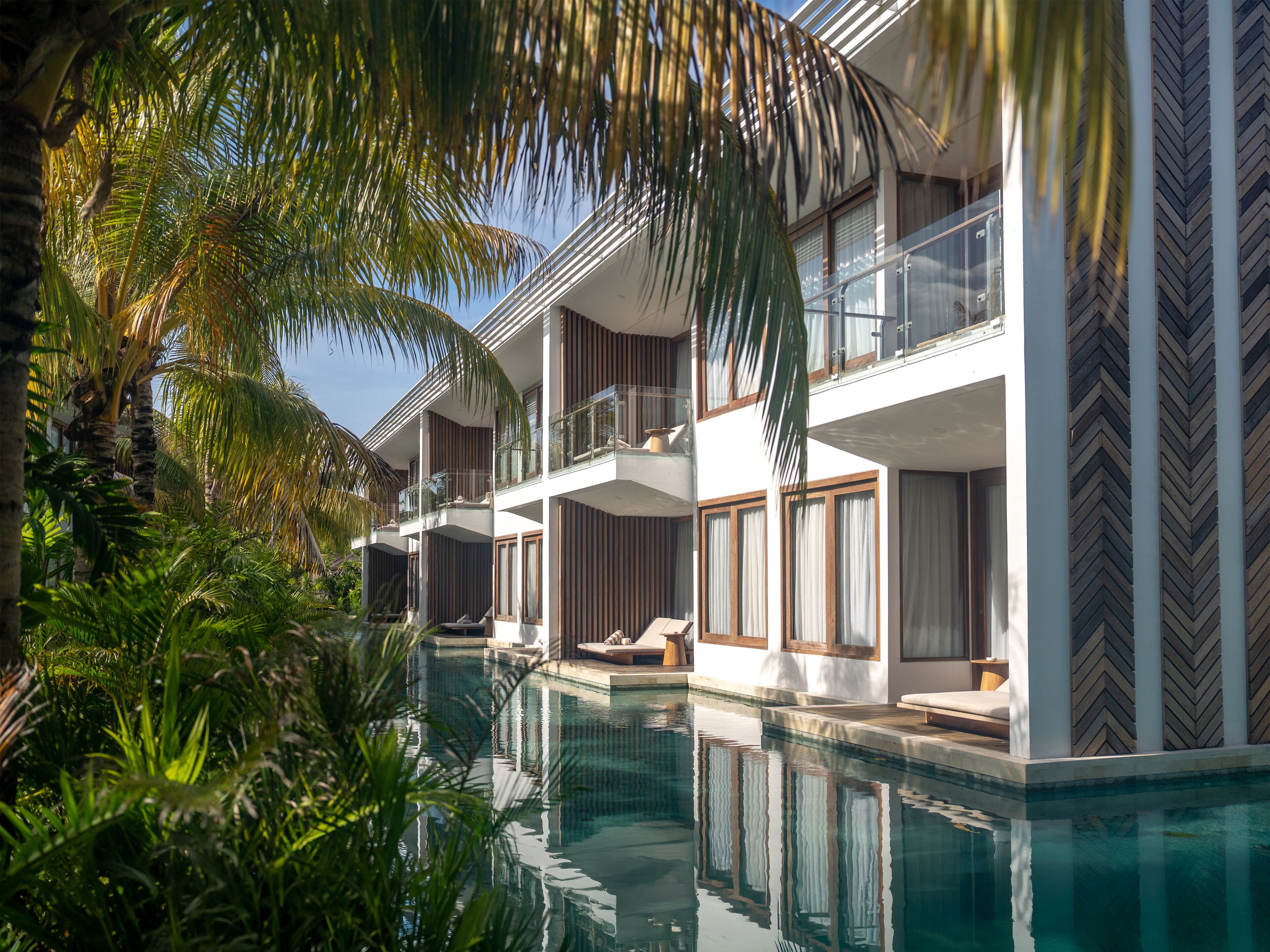 A modern hotel with a pool, balconies, and lush greenery.