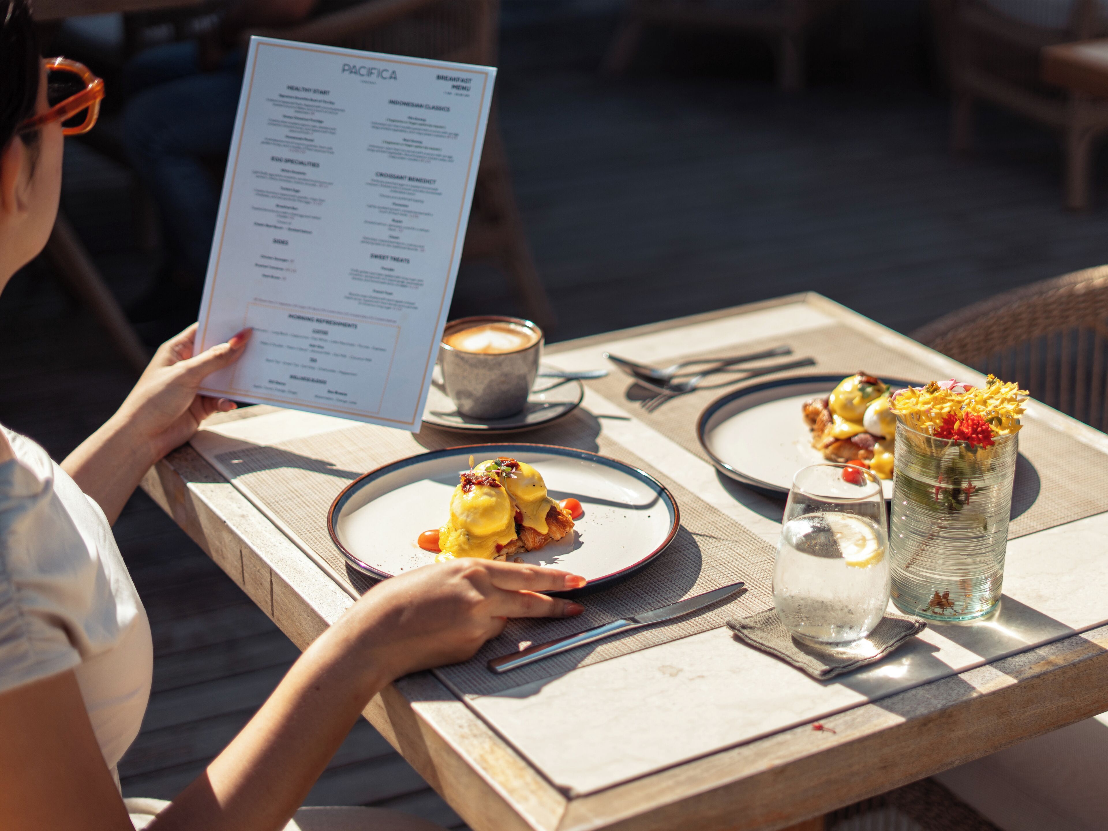 A menu with food items and a table with plates, cutlery, and a glass of water.