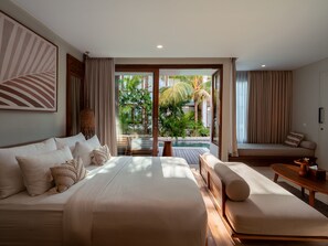 Habitación de hotel con una cama grande, un sofá, una mesa de comedor y vistas a una piscina y zonas verdes.