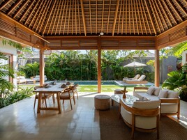 Un espacio al aire libre techado con piscina, sillones de descanso y una zona de comedor.