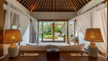 Una habitación con cama, lámparas de noche, mesita de noche y vistas a un área exterior con piscina y vegetación.