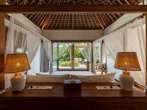Una habitación con cama, lámparas de noche, mesita de noche y vistas a un área exterior con piscina y vegetación.