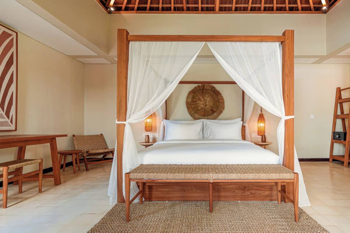 A four-poster bed with white curtains, wooden headboard, and bedside lamps.