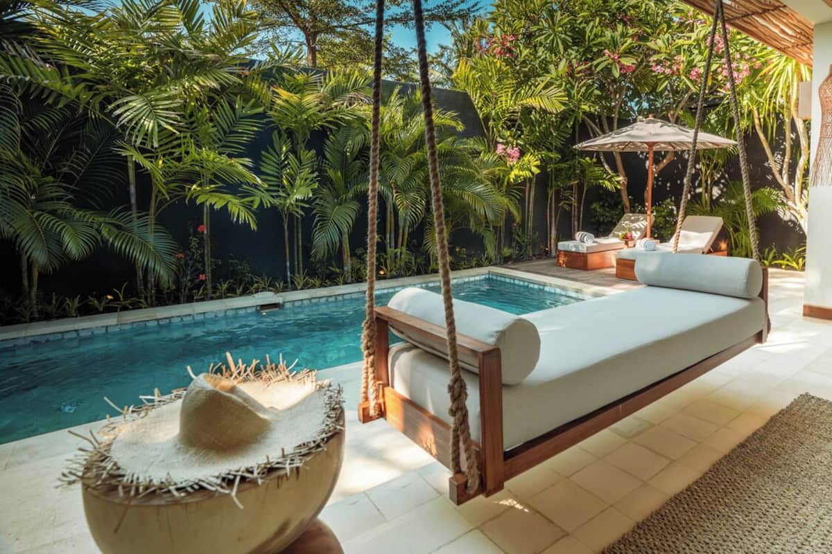A poolside area with a wooden swing chair, a lounge chair, and a hanging light fixture.