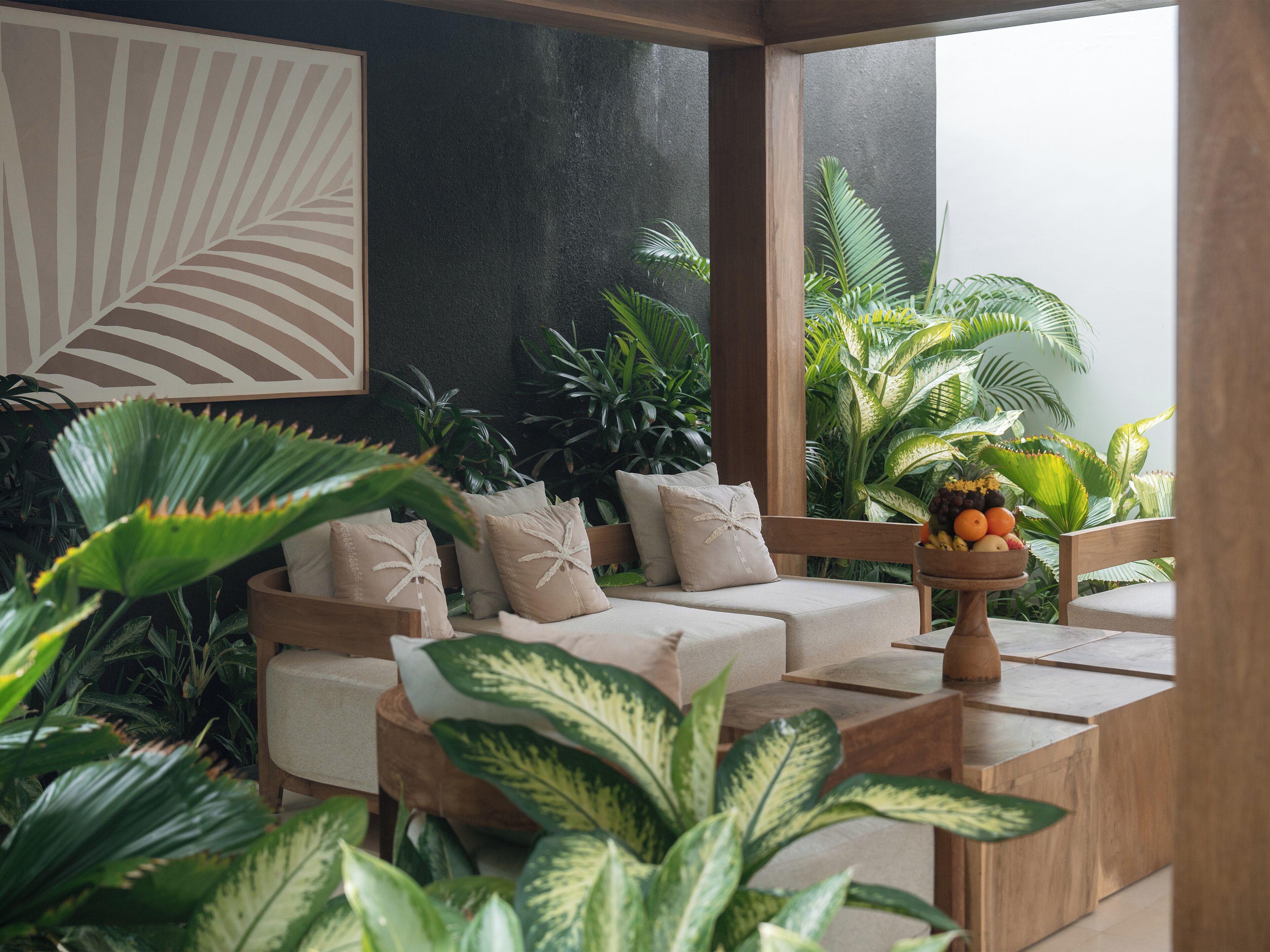 A modern living room with a sofa, a wooden coffee table with fruit, and lush green plants.