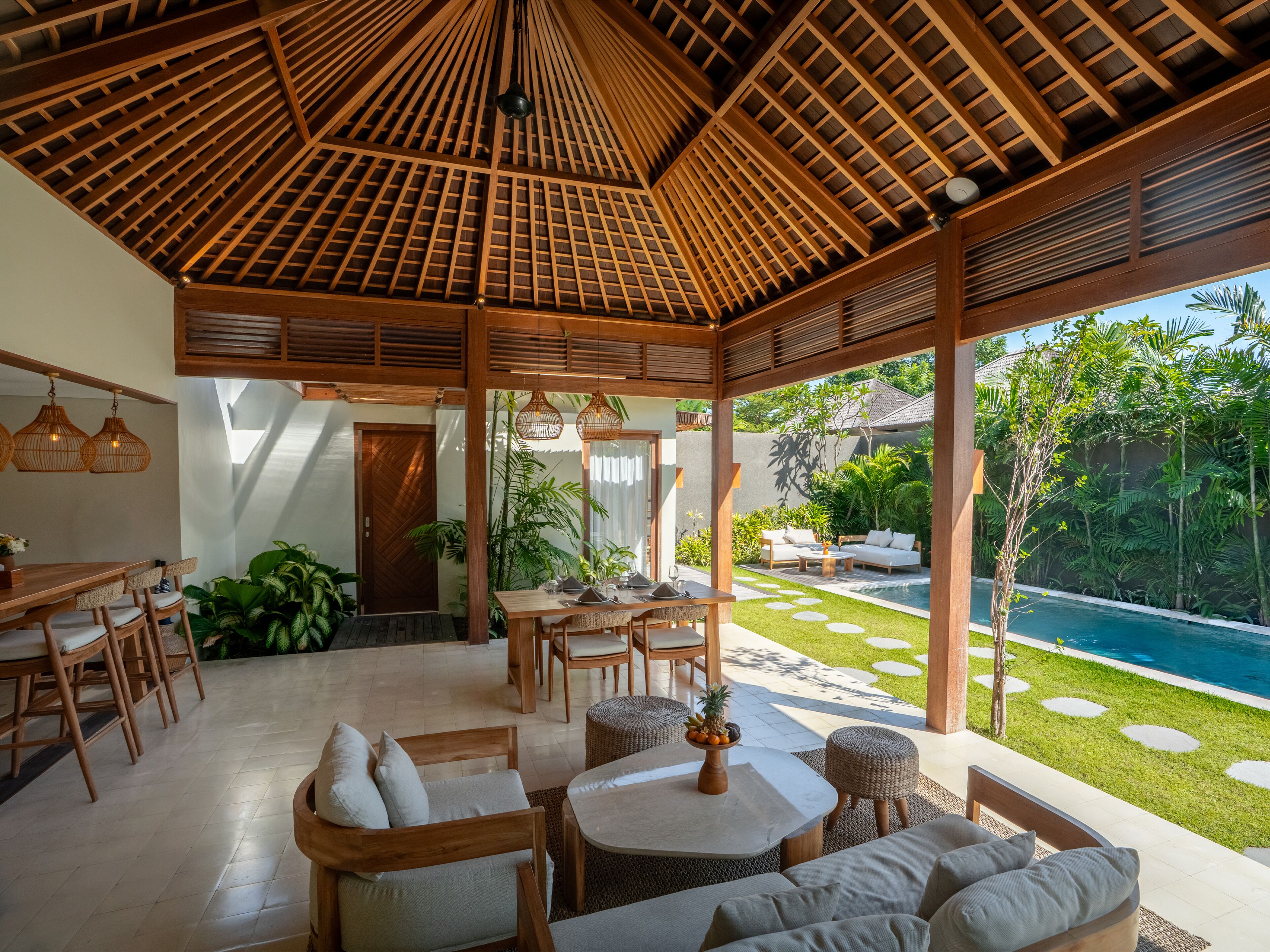 Un espace extérieur abrité, aménagé avec du mobilier en bois, une table à manger et offrant une vue sur une piscine.