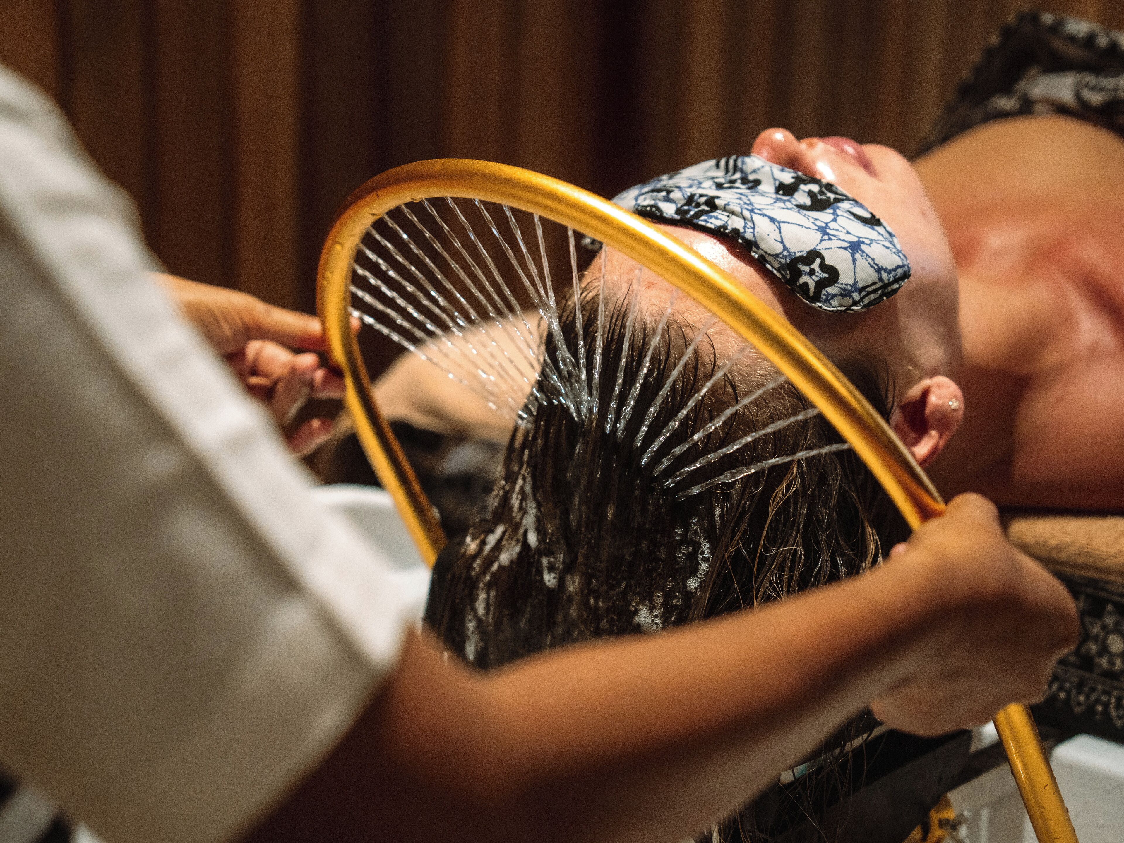 A person receiving a hair treatment with a mirror and a comb.